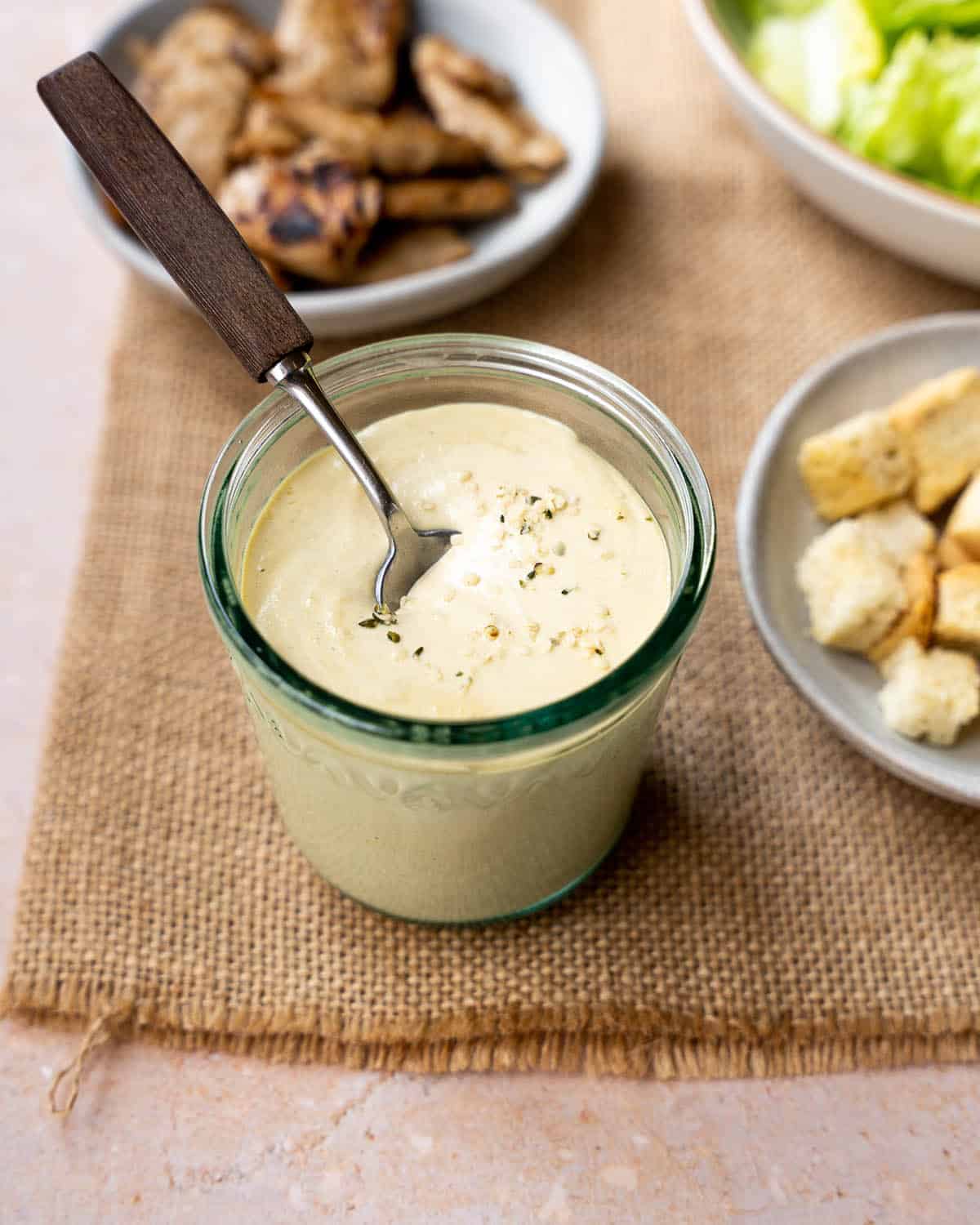 Cashew Caesar dressing in a glass jar with a spoon in it.