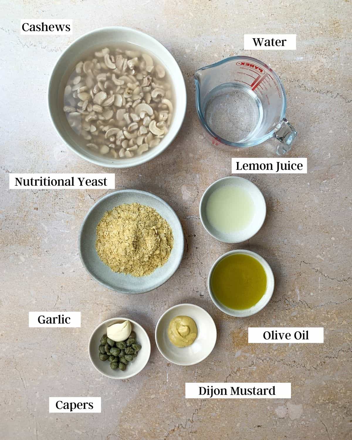 Ingredients for cashew caesar dressing in bowls on a marble surface.