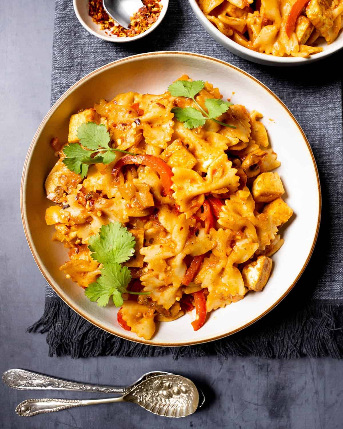 Curry pasta with tofu in a bowl with fresh herbs and chilli flakes.