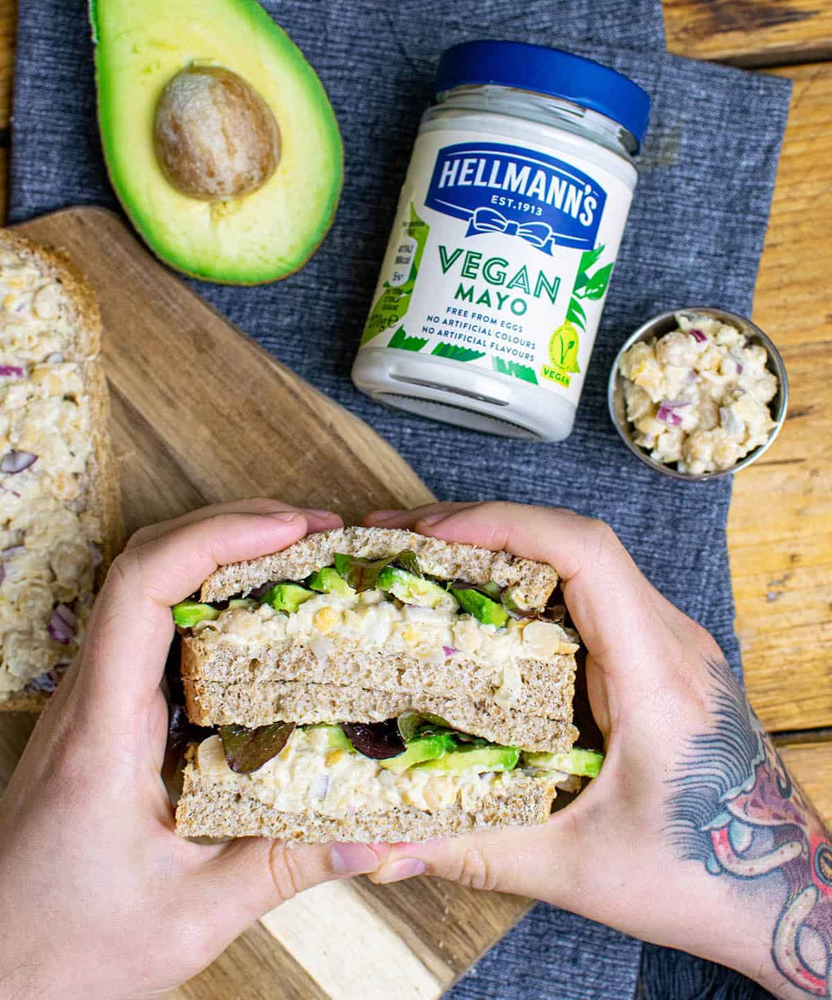 Chickpea tuna sandwich being held by a hand and with an avocado and a jar of Hellmanns mayo in the background