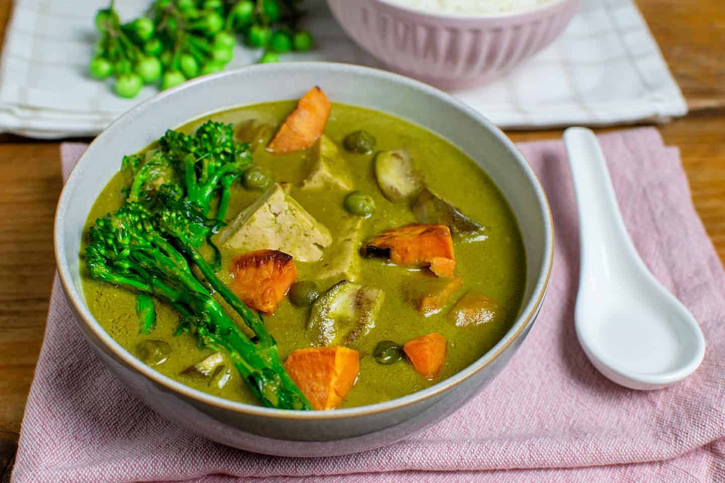 Vegan Thai Green Curry in a bowl with rice in the background and a spoon to the right