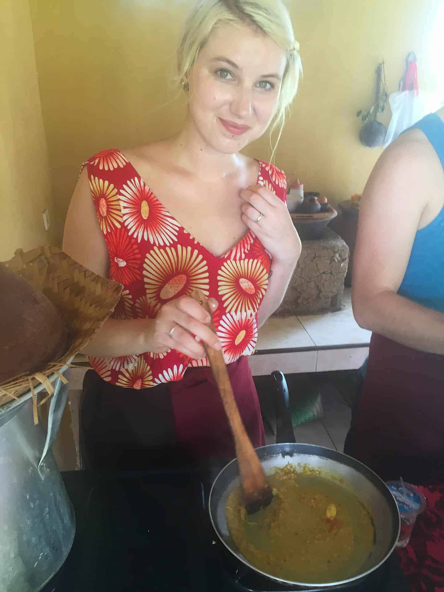 Jess at a cooking class in Bali, standing in front of a wok cooking a curry. She's wearing a red and yellow jumpsuit.