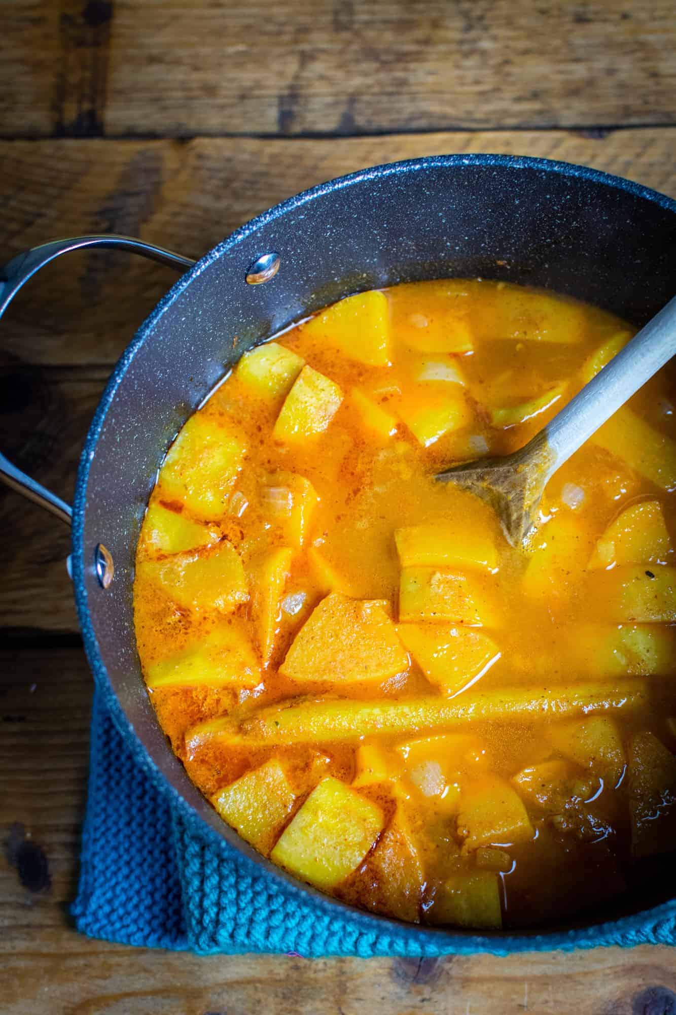 Soup pan containing pumpkin, coconut milk, veg broth, lemongrass and a wooden spoon