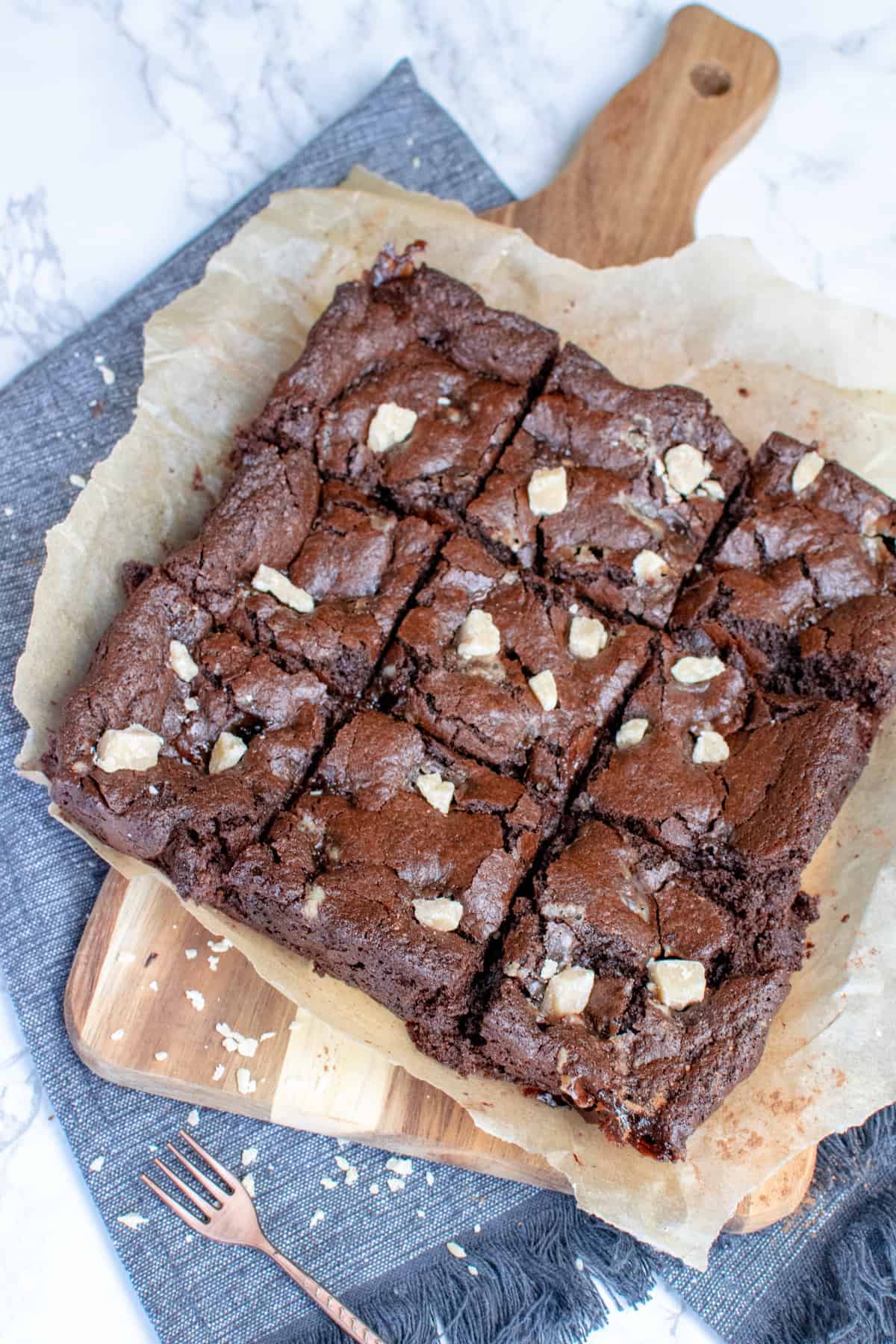 A big slab of vegan fudge brownie cut into smaller squares sat on top of a chopping board, which is on top of a blue towel.