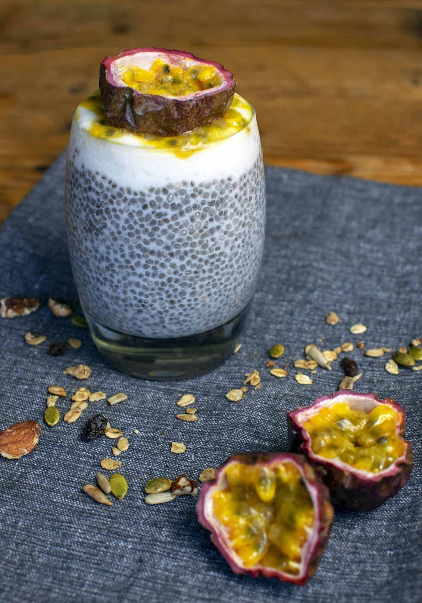 One passionfruit cut in half is in the foreground , with a glass full of chia pudding in the background, topped with half a passionfruit