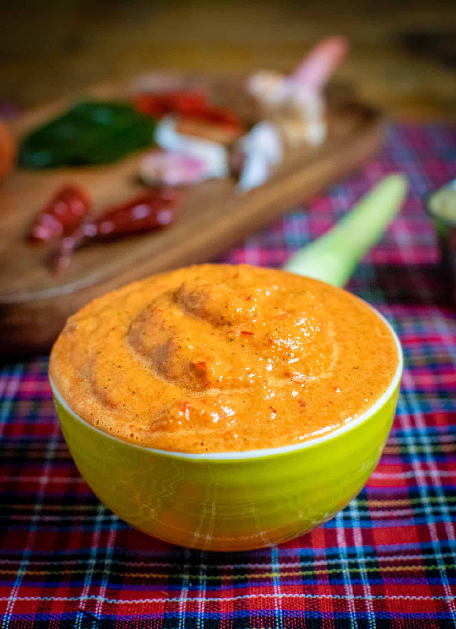 Vegan Thai red curry paste in a yellow bowl with lemongrass and other ingredients behind it