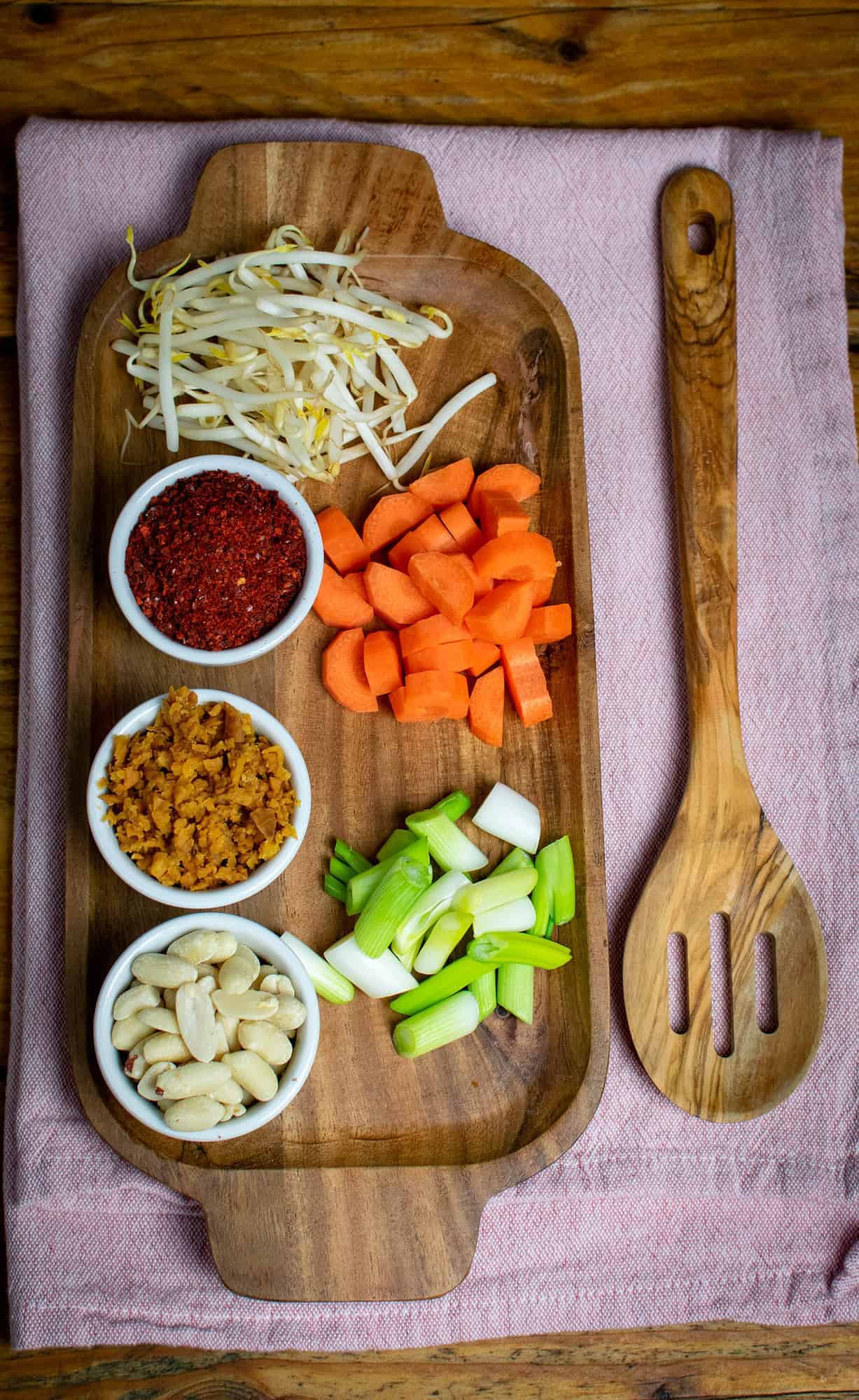 Pad Thai ingredients, chopped and prepared in small bowls, all sitting on a wooden serving board