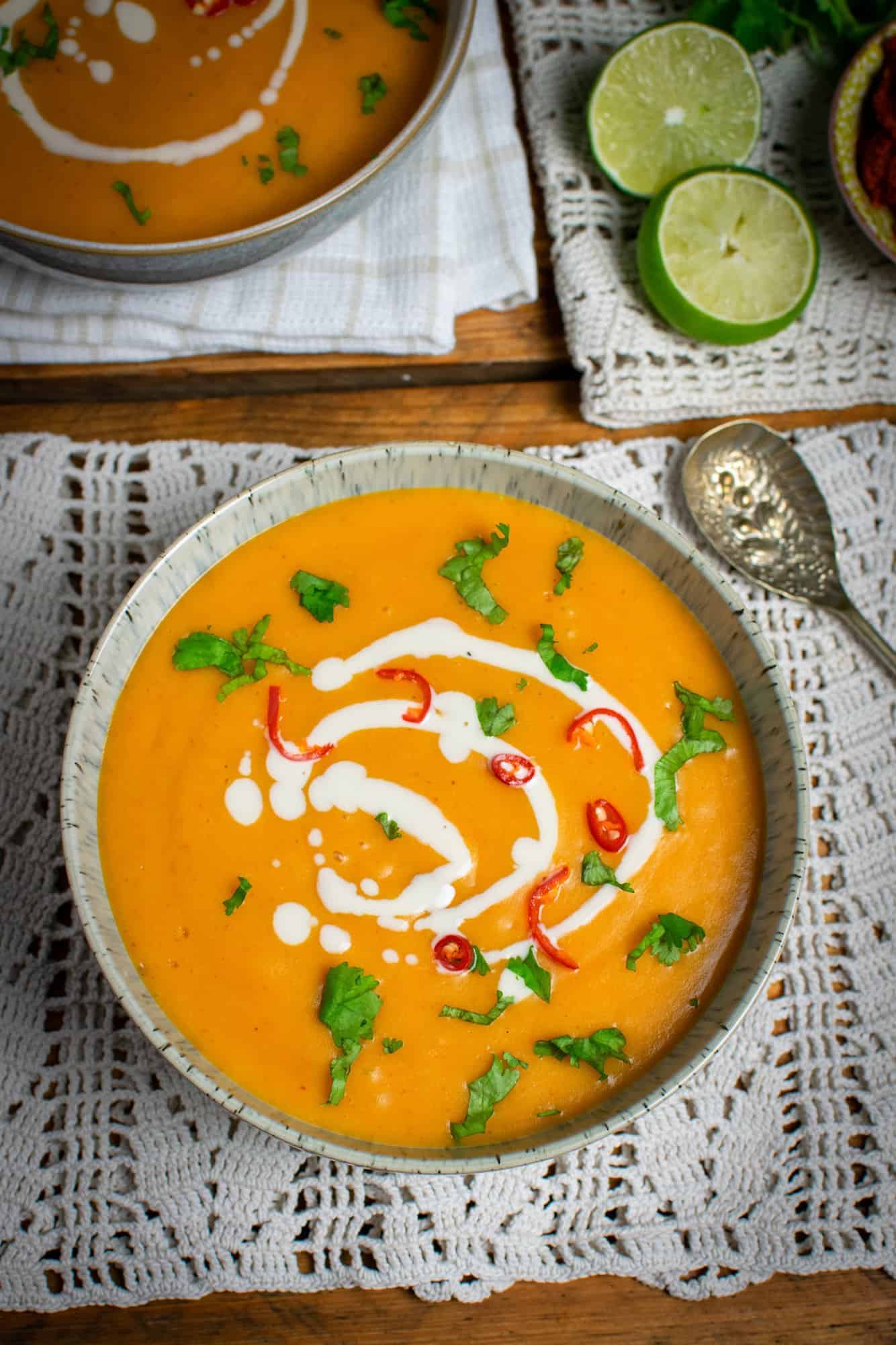 Orange pumpkin soup with Thai curry paste in a light bowl, with a spoon next to it and a lime in the background