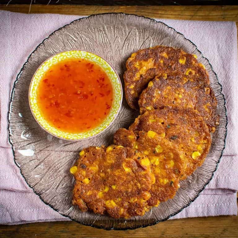 Glass plate of Corn Fritters next to a yellow pot of sweet chilli sauce