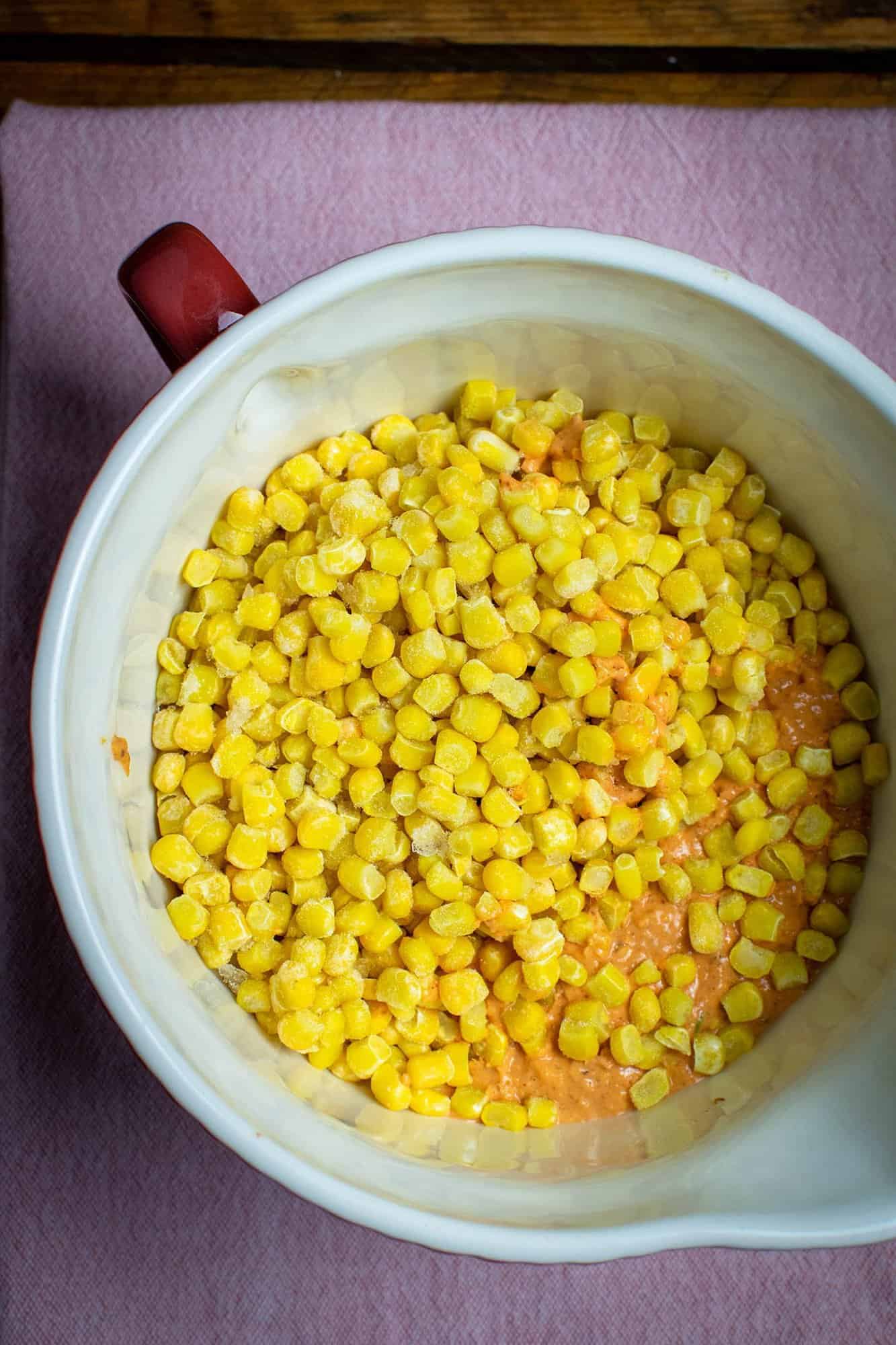 A mixing bowl full of sweetcorn and red batter mixture, ready to be mixed. Sat on a pink tea towel.