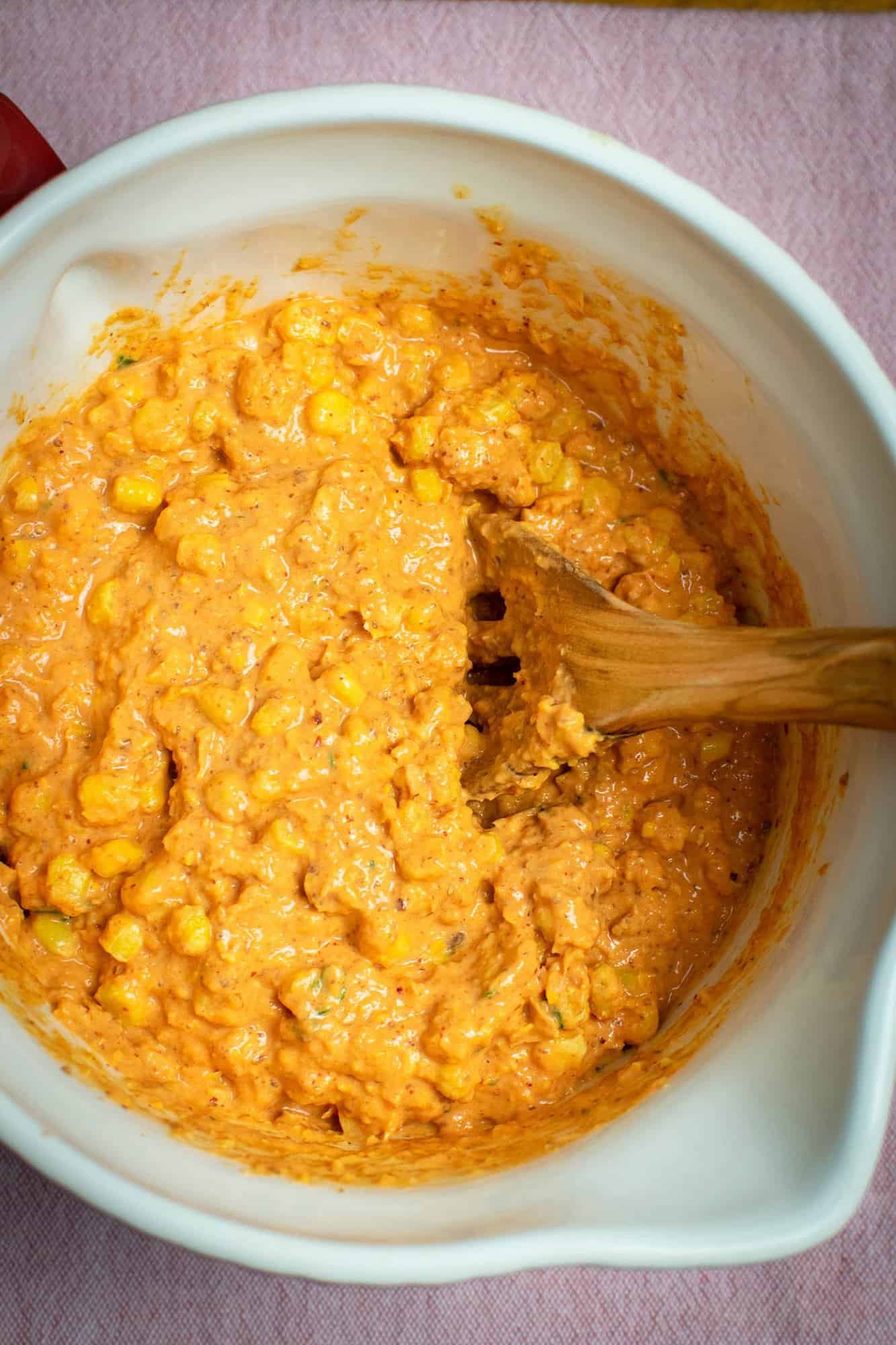 A mixing bowl full of corn fritter batter fully mixed with a wooden spoon in it.