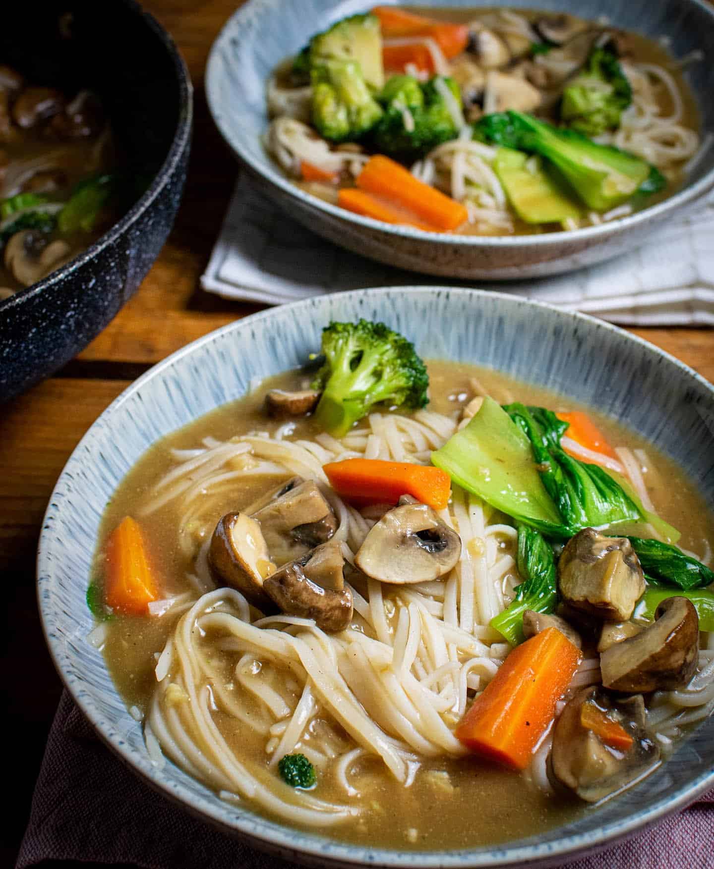 Rad na noodles in a white blue bowl and a grey wok to the left.