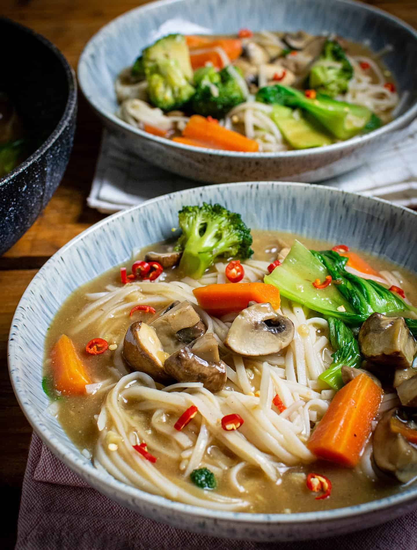 Rad Na noodles with mushrooms, broccoli and pak choi in a blue bowl. The noodles and gravy sauce are also visible.