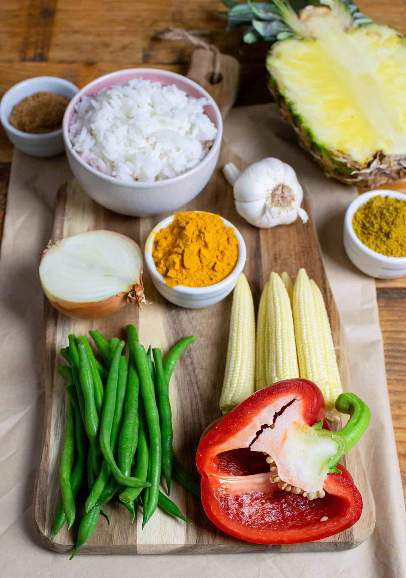 A load of ingredients including rice, veggies, turmeric and garlic laid out on a chopping board.