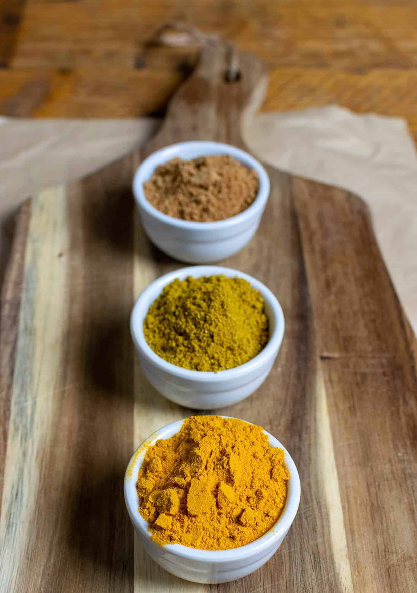 3 pots laid out on a chopping board that contain sugar, curry powder and turmeric powder