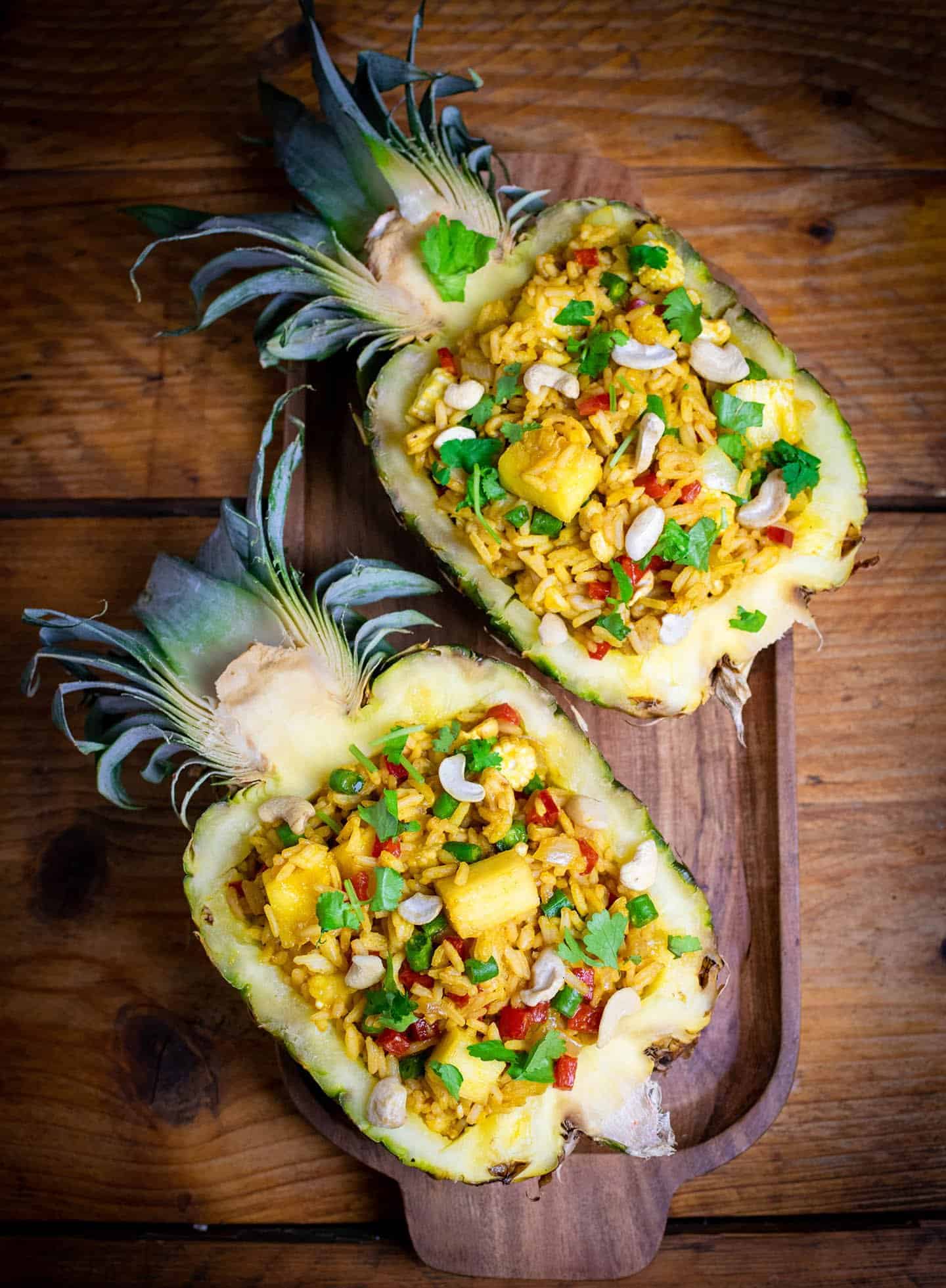 Dos mitades de piña rellenas de arroz, sentadas en una bandeja de madera.