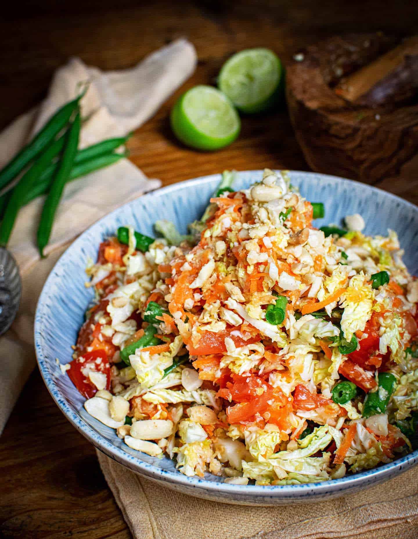 Portrait photo showing vegan papaya salad in a blue bowl sat on an orange cloth, with a pestle and mortar in the top right hand corner