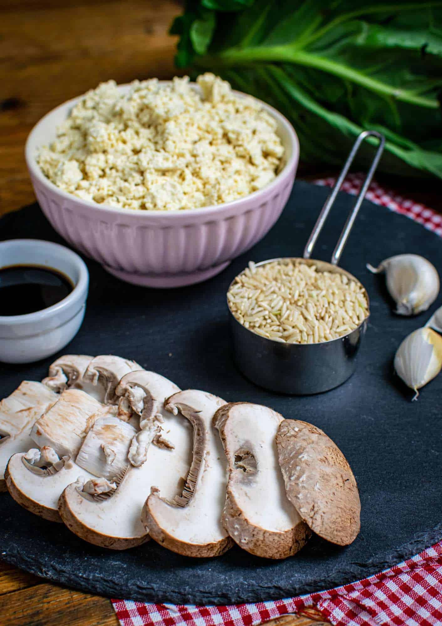 Rice, mushrooms, garlic, soy sauce and crumbled tofu laid out on a round slate.