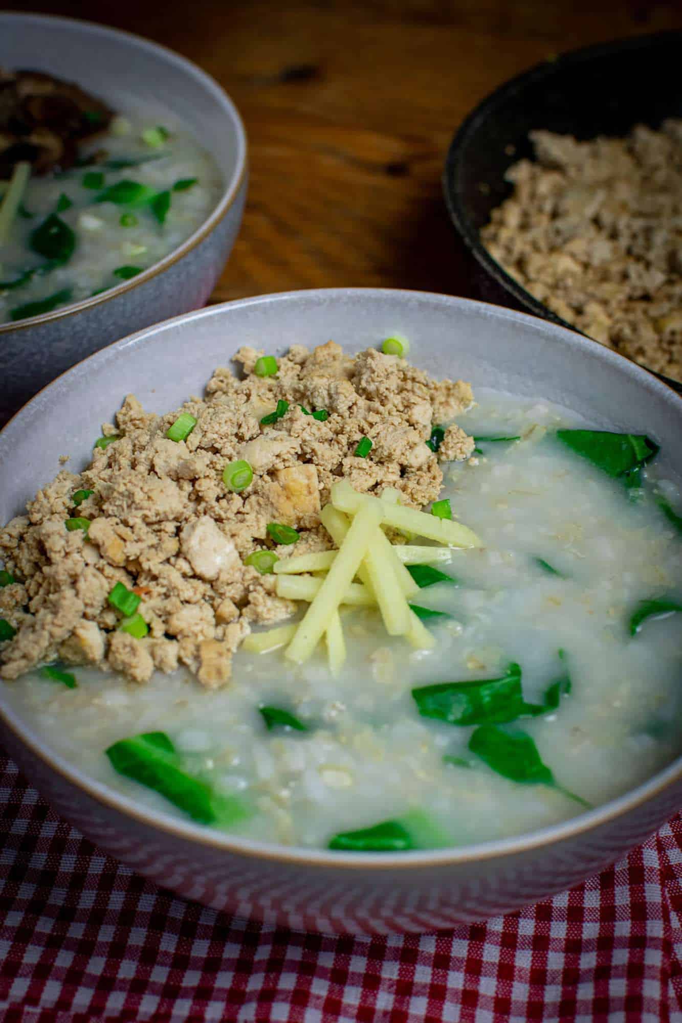 A big bowl of Thai jok with wilted spring greens, topped with fried tofu and fresh ginger