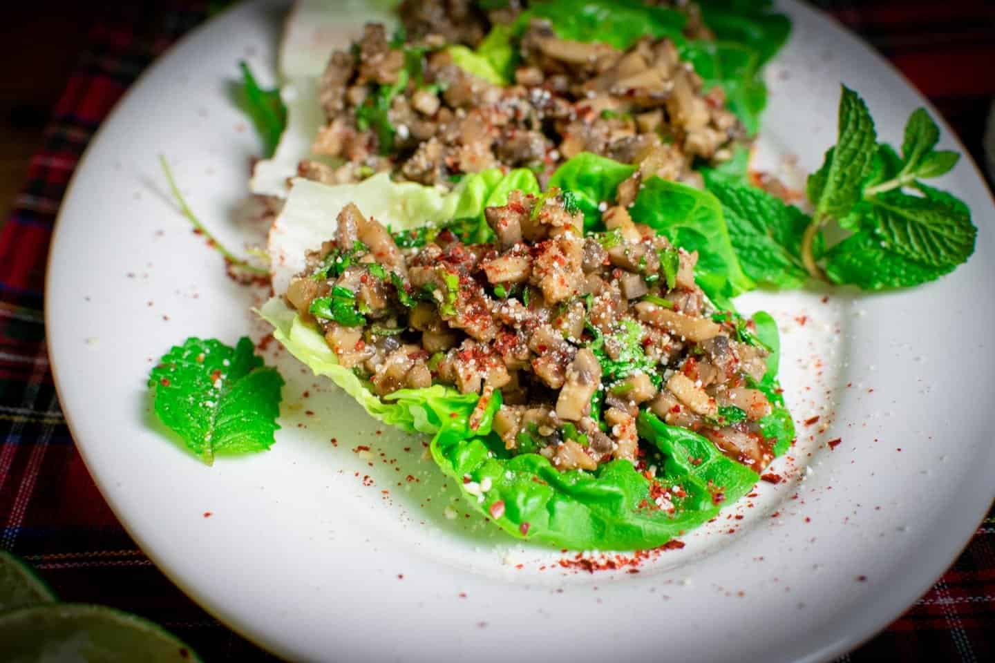 A white oval dish with larb on it with mint leaves scattered for decoration