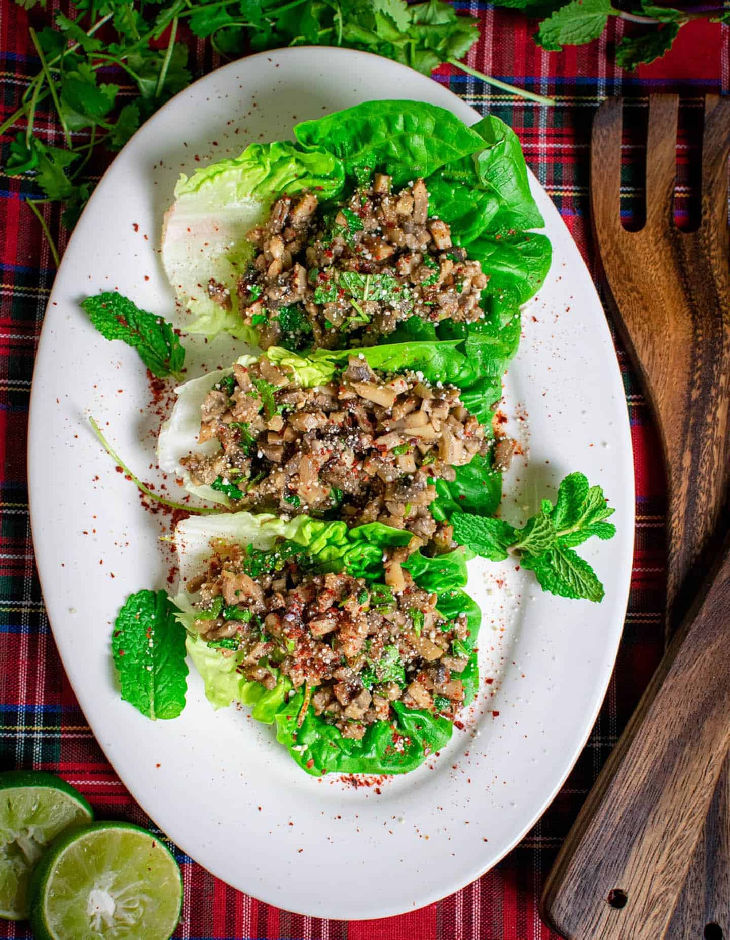 On a white oval plate there's 3 baby gem lettuce leaves filled with salad and there are mint sprigs around the outside