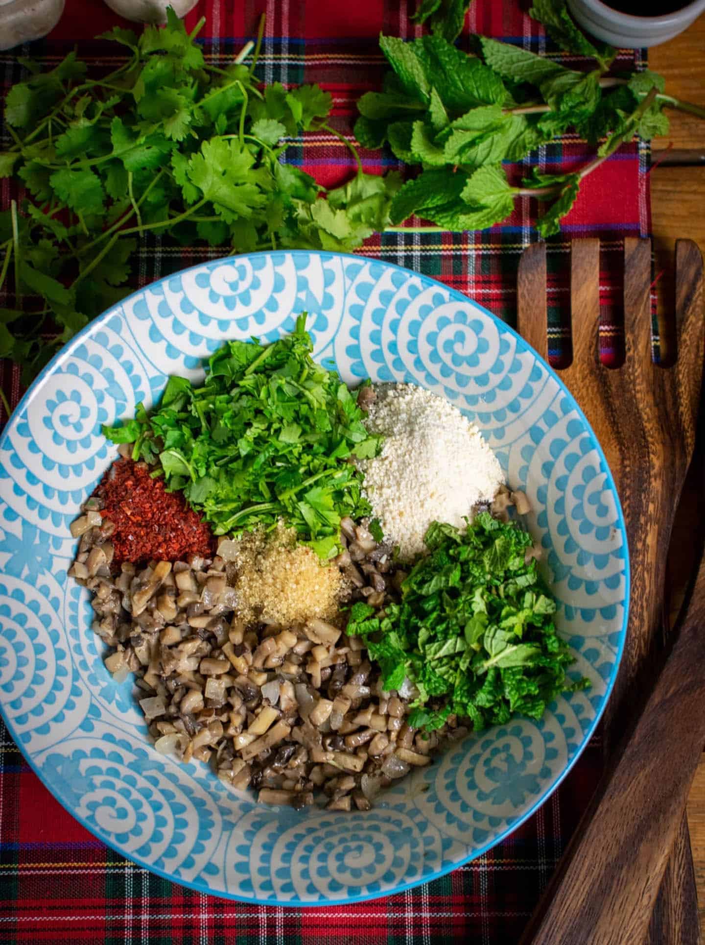 In a large blue bowl there is some cooked off diced mushrooms, fresh coriander, roasted rice, fresh mint, sugar and chilli flakes