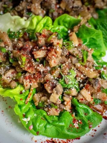 Square photo of mushroom larb on a leaf of baby gem sprinkled with chilli flakes