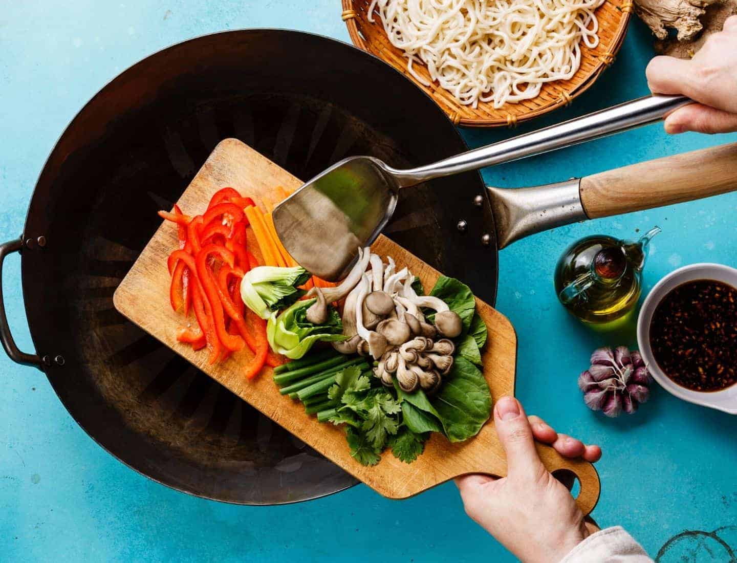 Blue background with a wok on it and a chopping board with veg on it hovering over the wok about to be put in the pan.