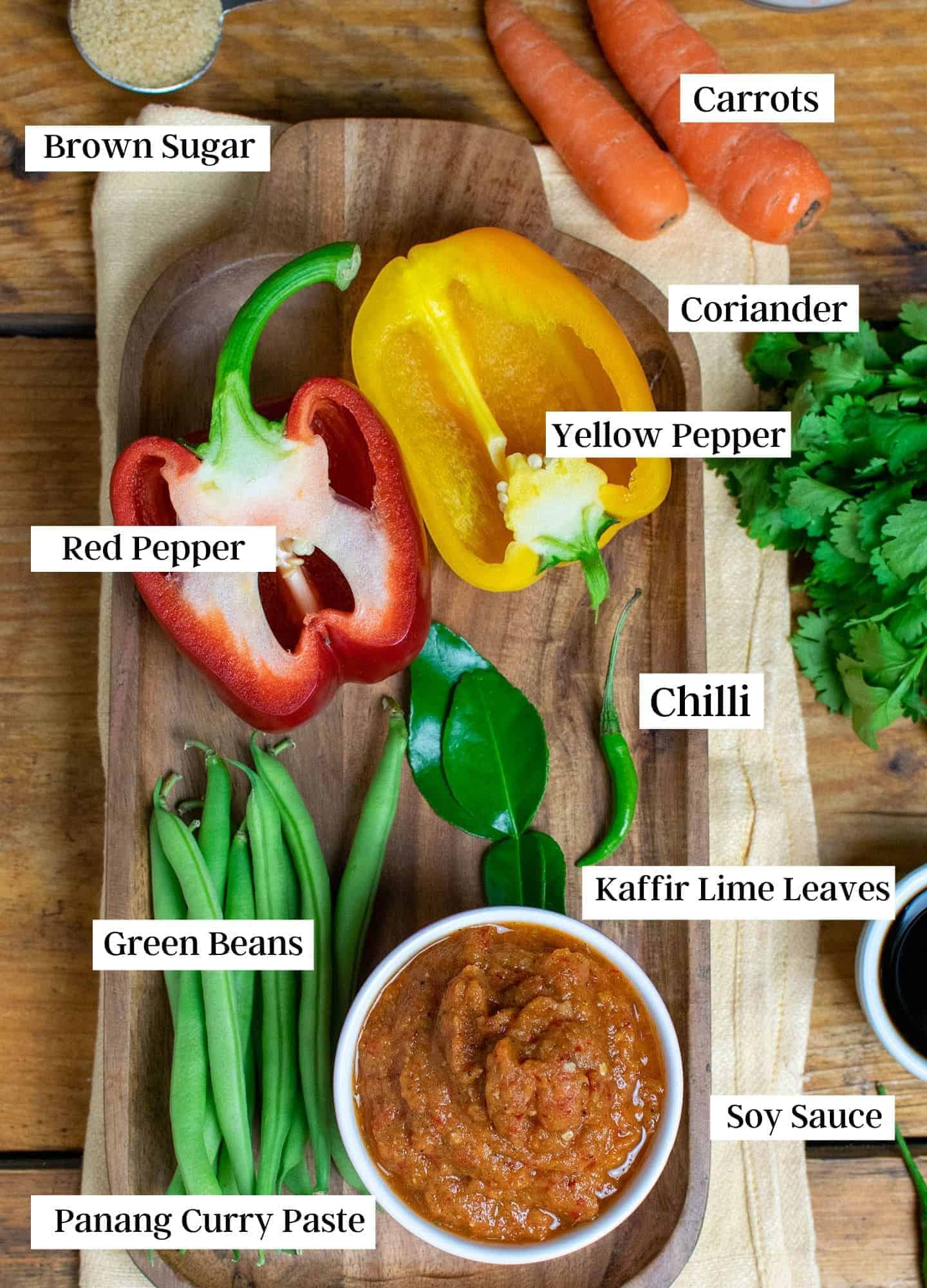 Ingredients laid out on a wooden board showing carrots, peppers, green beans and curry paste