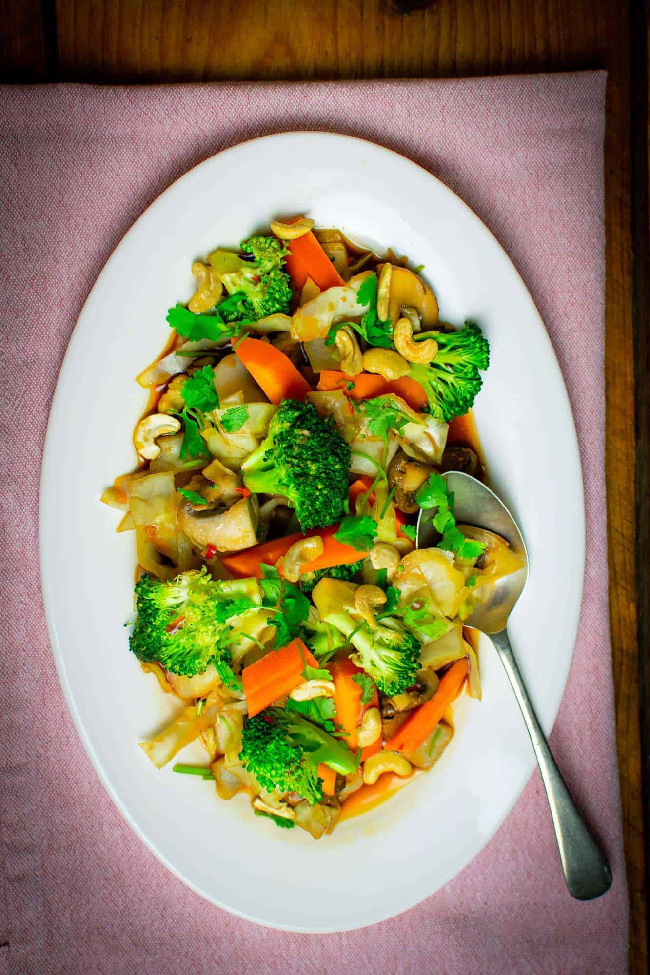 Top down view of the veggie stir fry on a pink background with a spoon balanced on the plate on the right. 