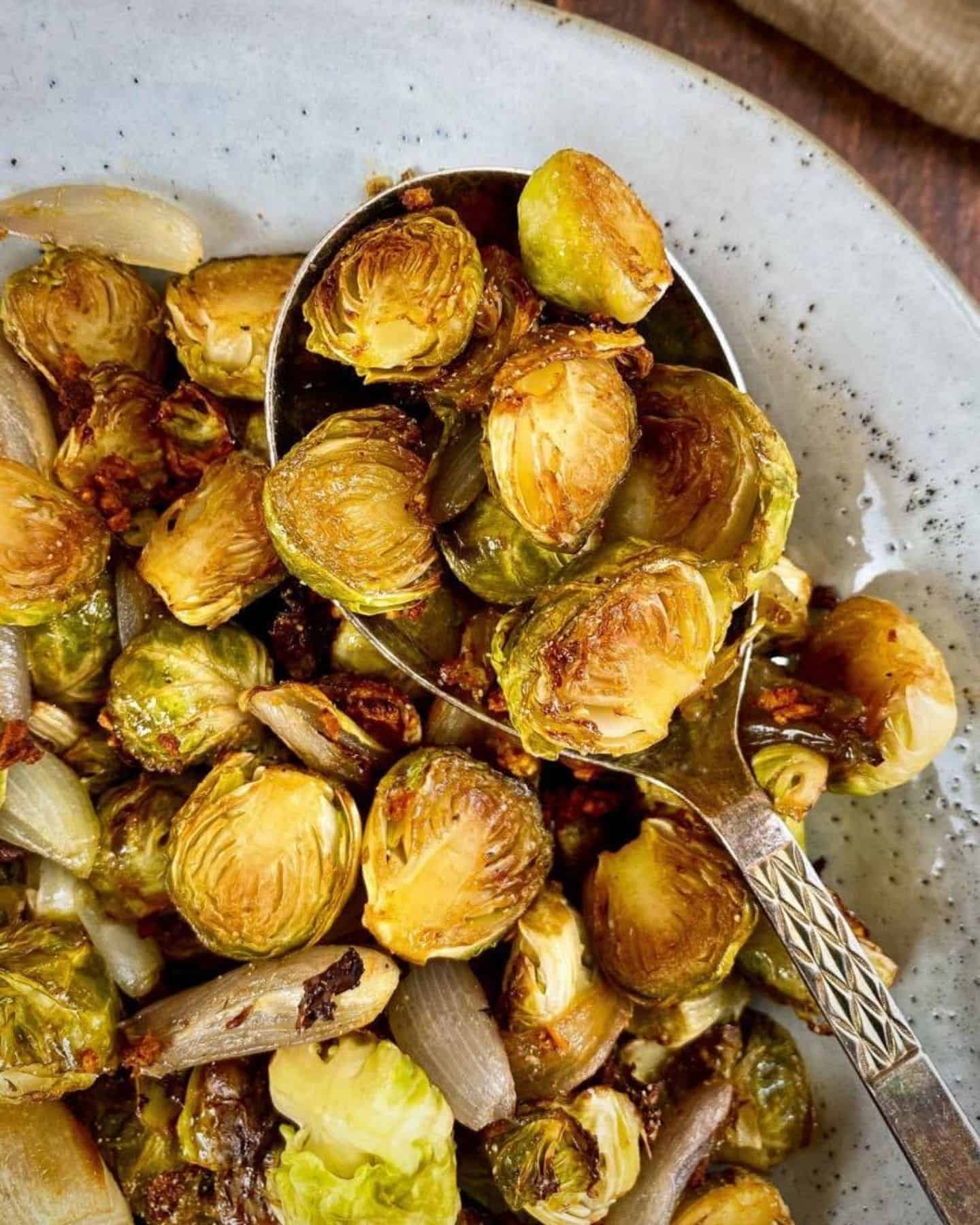 Brussels sprouts on a white plate and some of the sprouts are balanced on a serving spoon