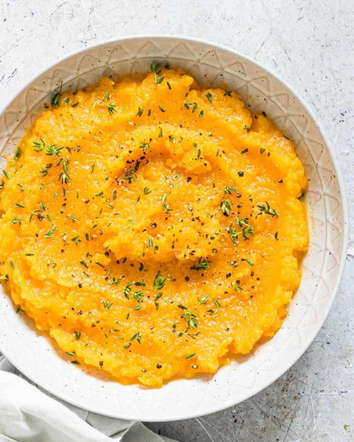 Butternut squash in a white bowl with green herbs on top