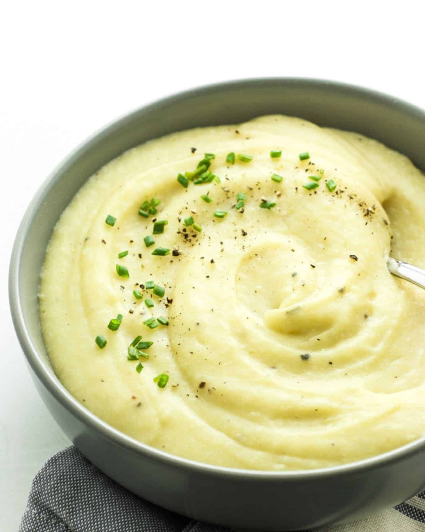 Creamy cauliflower and potato mash in a grey bowl and with a spoon in it