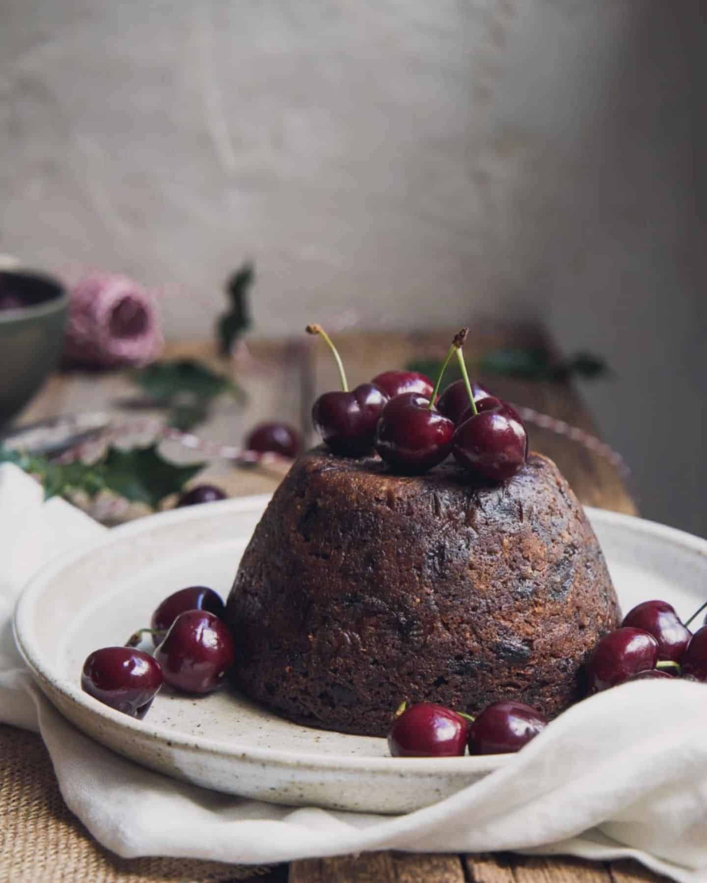 Christmas pudding on a white plate with cherries on top