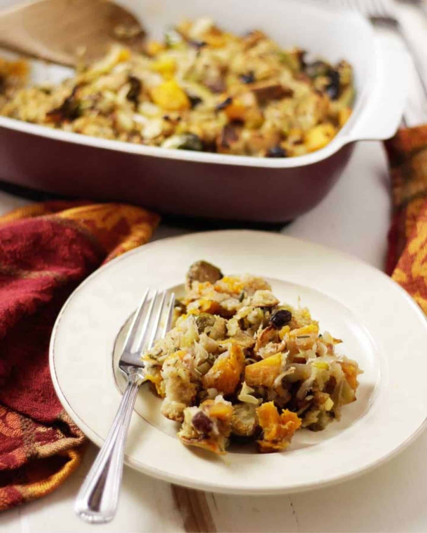 Stuffing on a plate with a fork and a oven dish is full of stuffing in the background