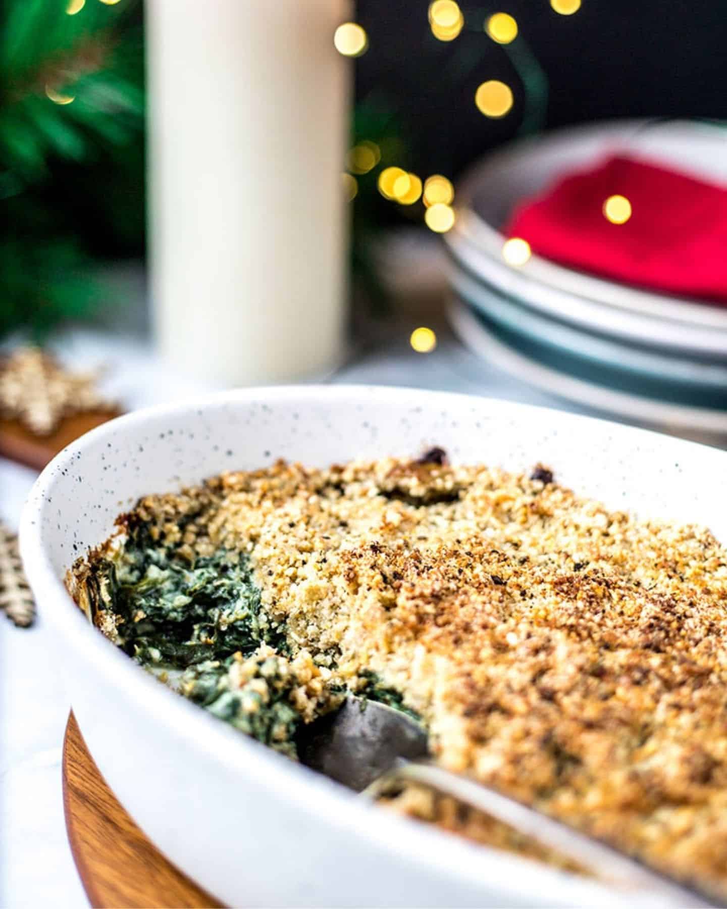 Creamed spinach gratin in an oven dish with a candle and Christmas tree branches in the background