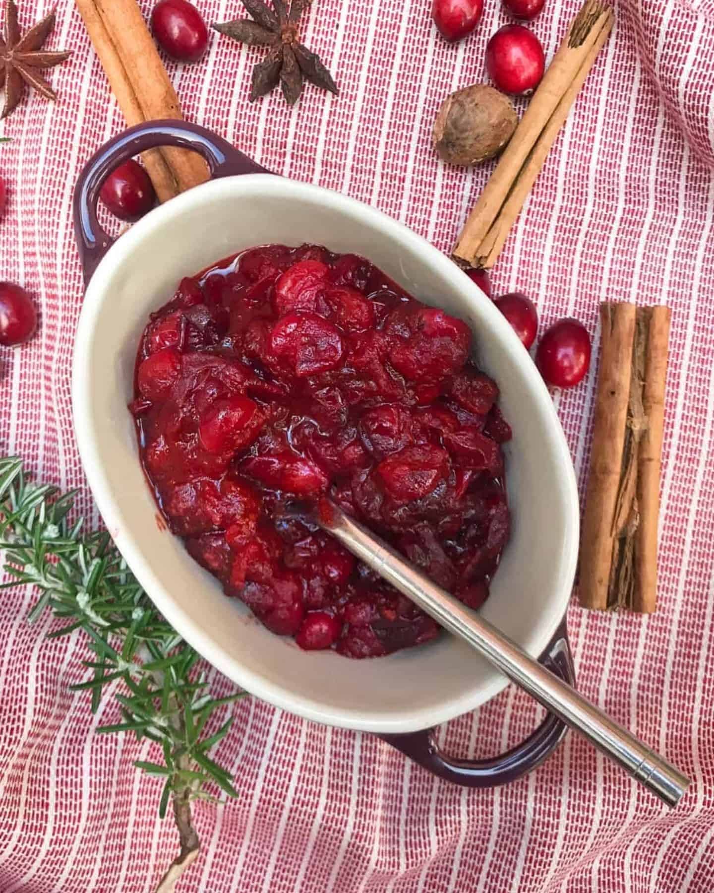 Cranberry sauce in an oval dish on a red background with cinnamon and berries beside it