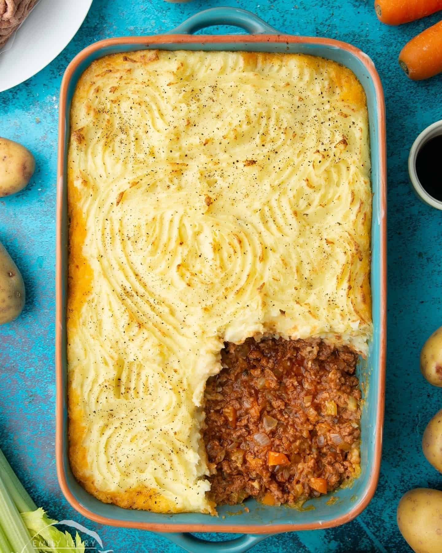 Vegan cottage pie in a large oven dish with a slice cut out in the right bottom corner so the filling is visible