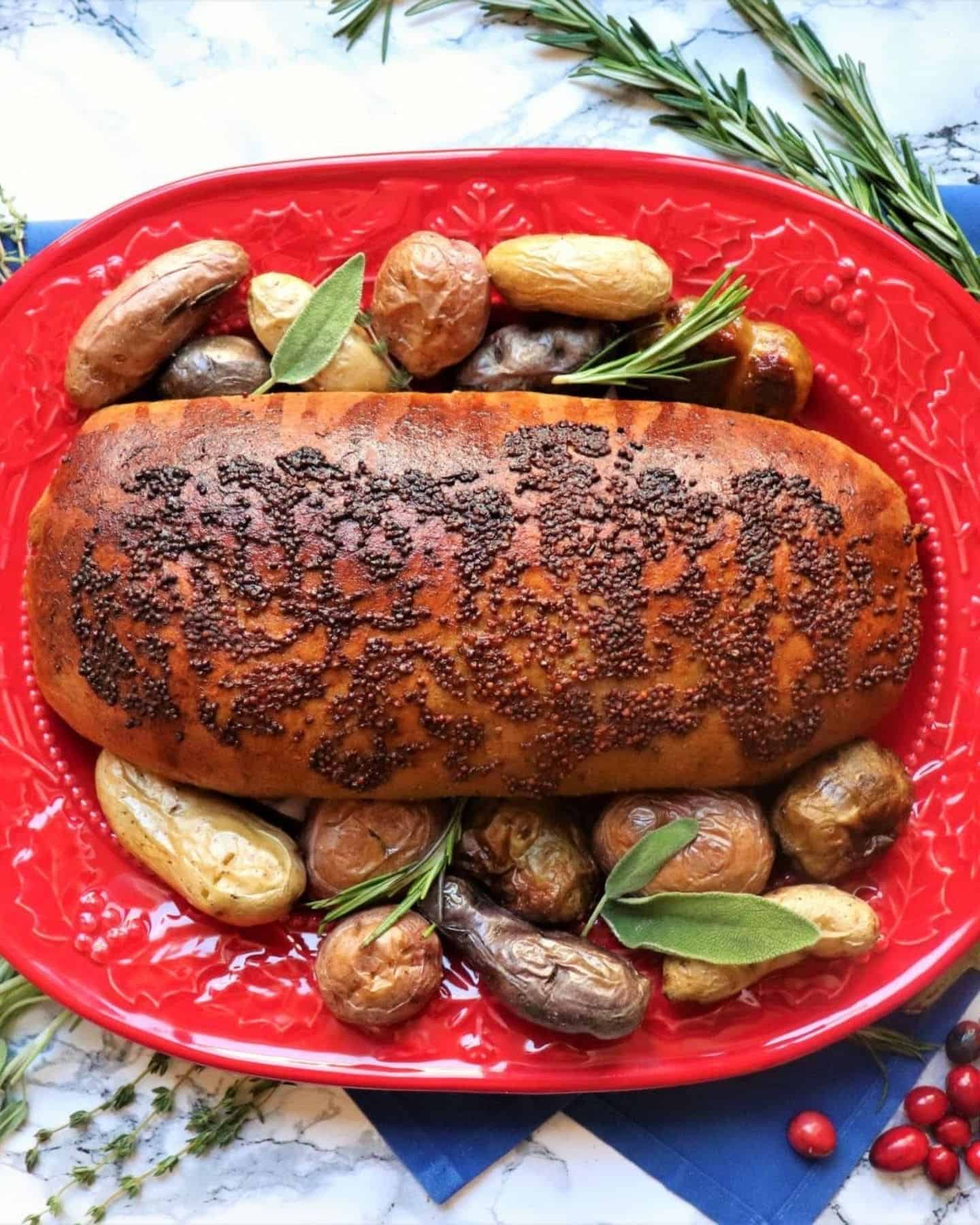 Stuffed seitan on a red vegan CHristmas dinner platter with potatoes and sage around the outside