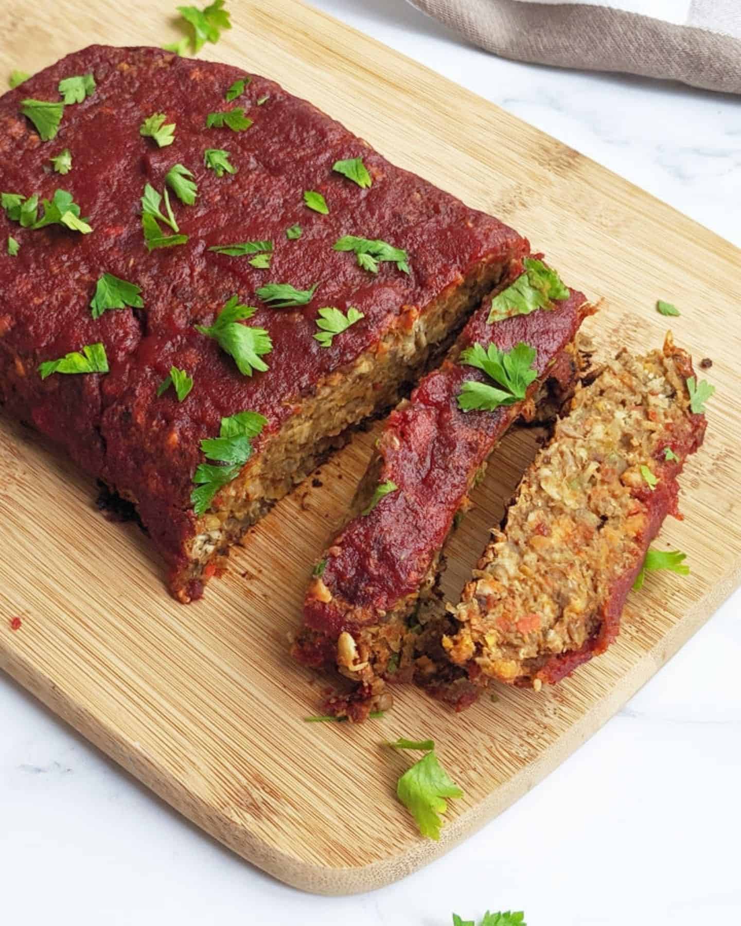 Lentil loaf on a chopping board with a red sauce on top of it and two slices cut away