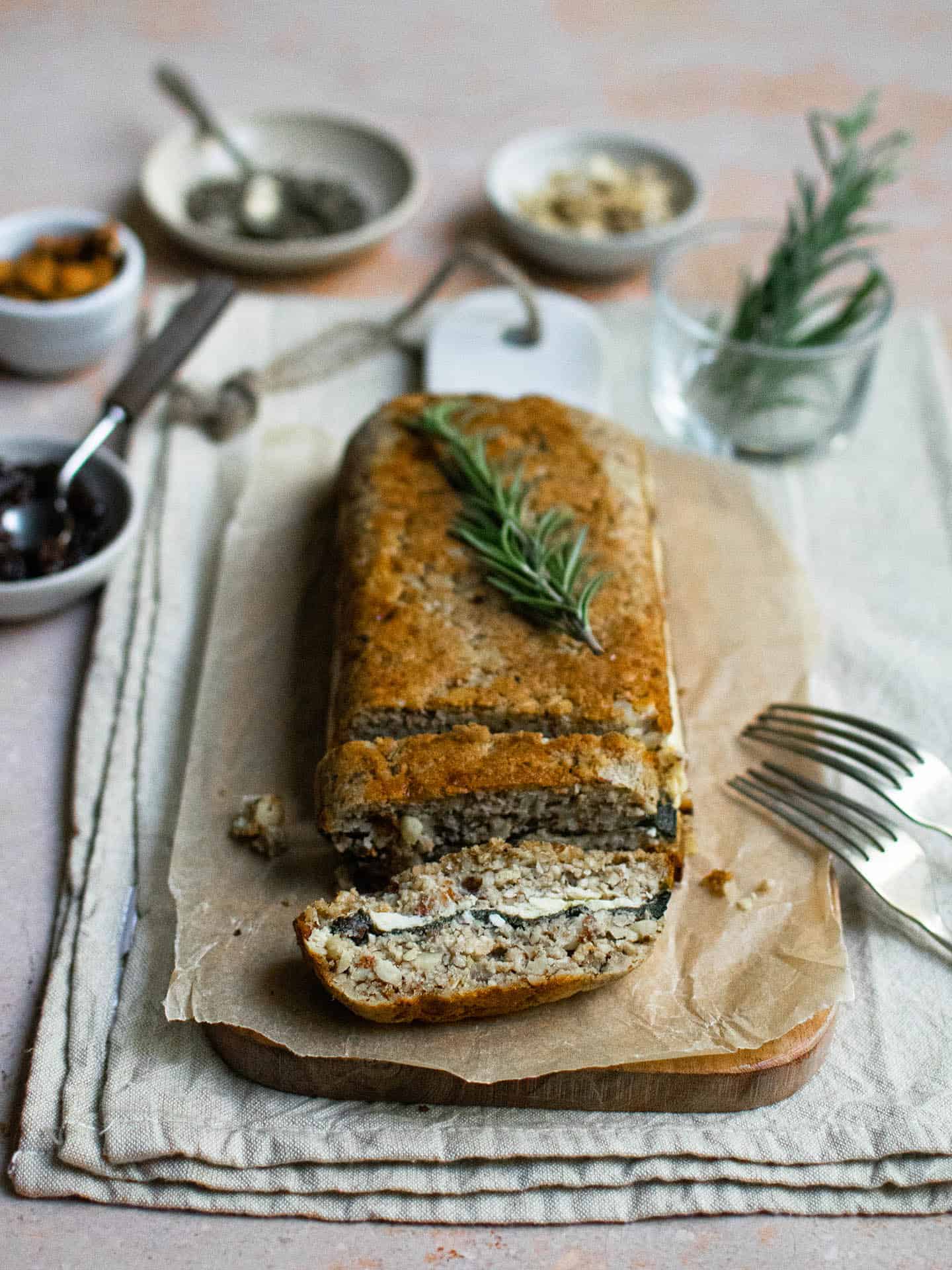 A cashew nut roast sat on some parchment paper, with two slices cut into it. The closest slice is laying on its side which shows a layer of spinach and cheese running through the middle.