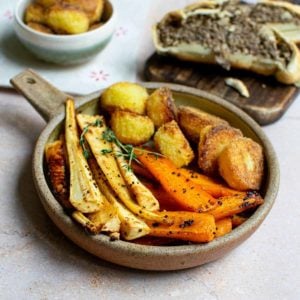 Carrots, parsnips and potatoes plated in a bowl with a handle with other dishes in the background