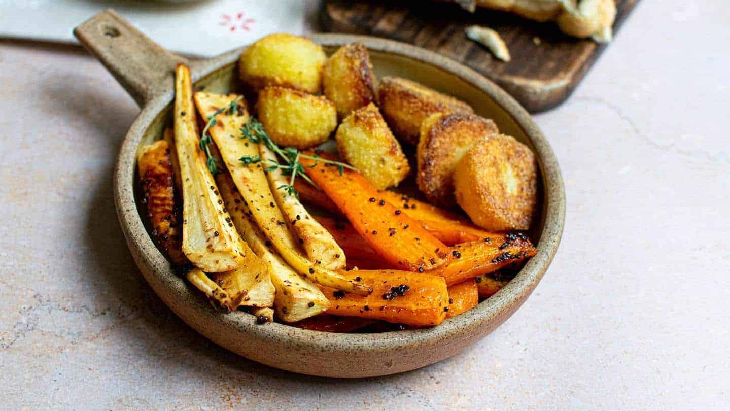 Landscape image of maple roasted carrots and parsnips with roast potatoes and sprigs of thyme on top