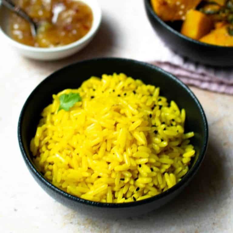 A black bowl filled with golden pilau rice. Some black nigella seeds and a bit of fresh coriander are scattered on the rice.