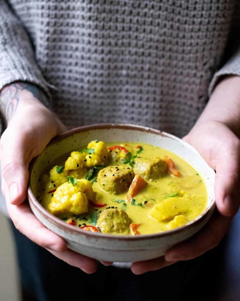 Dan's hands holding a bowl of yellow korma. Falafel, peppers and cauliflower can all be seen.