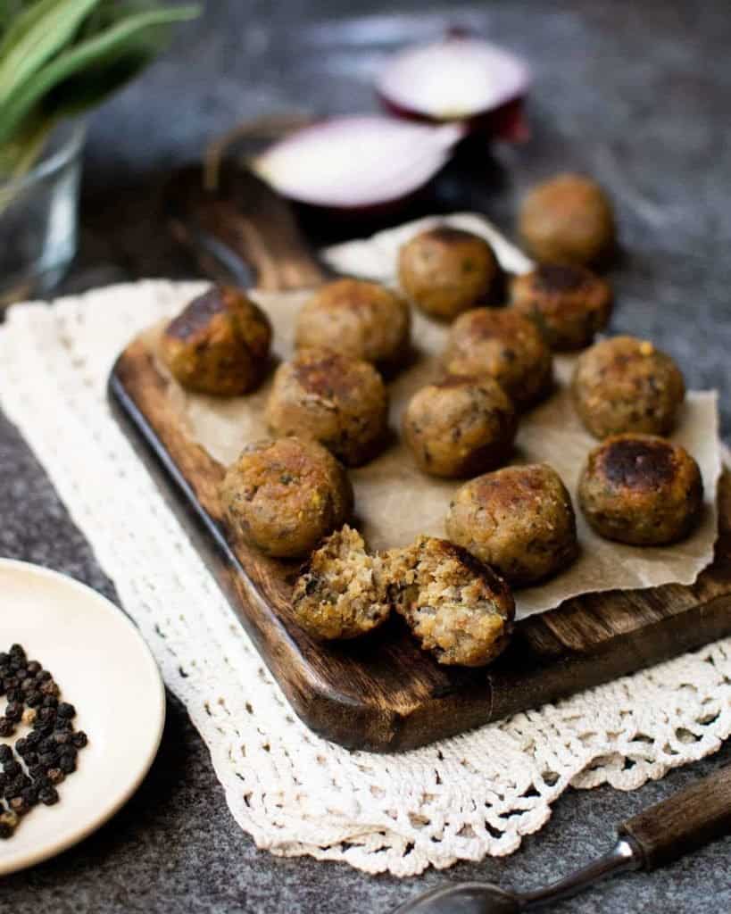 Vegan stuffing balls on a chopping board with herbs to the back right in a glass ramekin