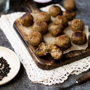 A chopping board full of stuffing balls made using the best sage and onion stuffing recipe. There's a small bowl of peppercorns to the left and a spoon in the foreground to the right