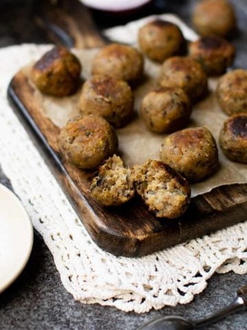 A chopping board full of stuffing balls made using the best sage and onion stuffing recipe. There's a small bowl of peppercorns to the left and a spoon in the foreground to the right