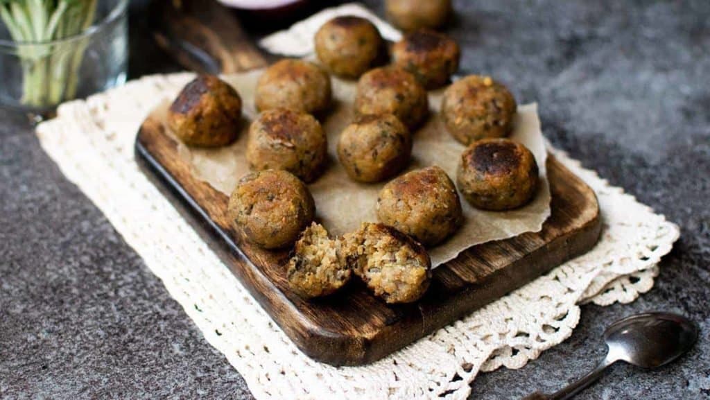 Sage and onion stuffing balls on a chopping board with a cream patterned cloth underneath and a spoon in the foreground to the right