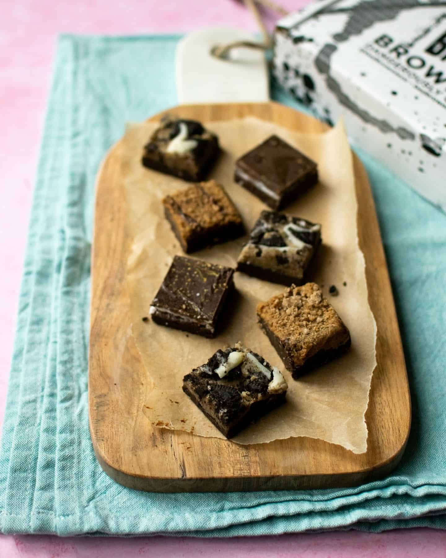 7 vegan chocolate brownies are laid out on a wooden board. The front one visibly has Oreo cookie pieces on it.